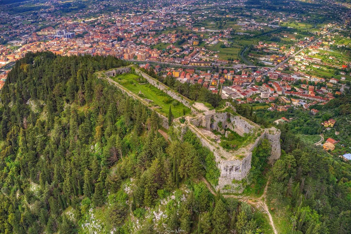 Le rovine del castello di Sora sulla cima di un colle boscato, con la città dai tetti rossi nella valle sottostante