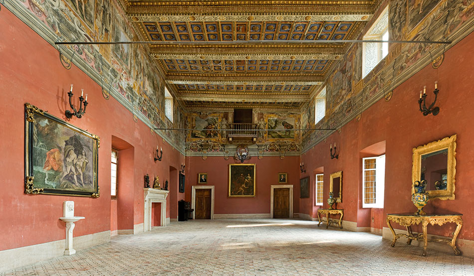 Salone interno del Castello Boncompagni di Isola del Liri con pareti color terracotta, soffitto a cassettoni dorati e blu, fregio affrescato, console rococò e pavimento a mosaico