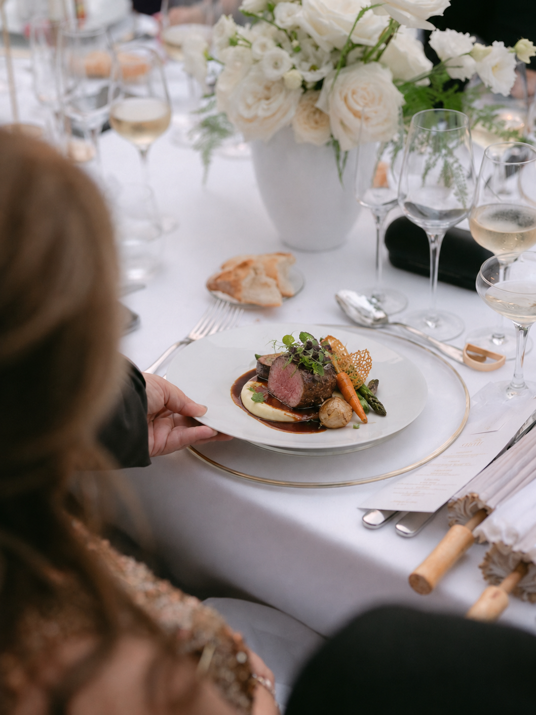 Piatto del menu di matrimonio servito a tavola durante un ricevimento a Villa Sant'Erasmo, con fiori bianchi, calici e pane