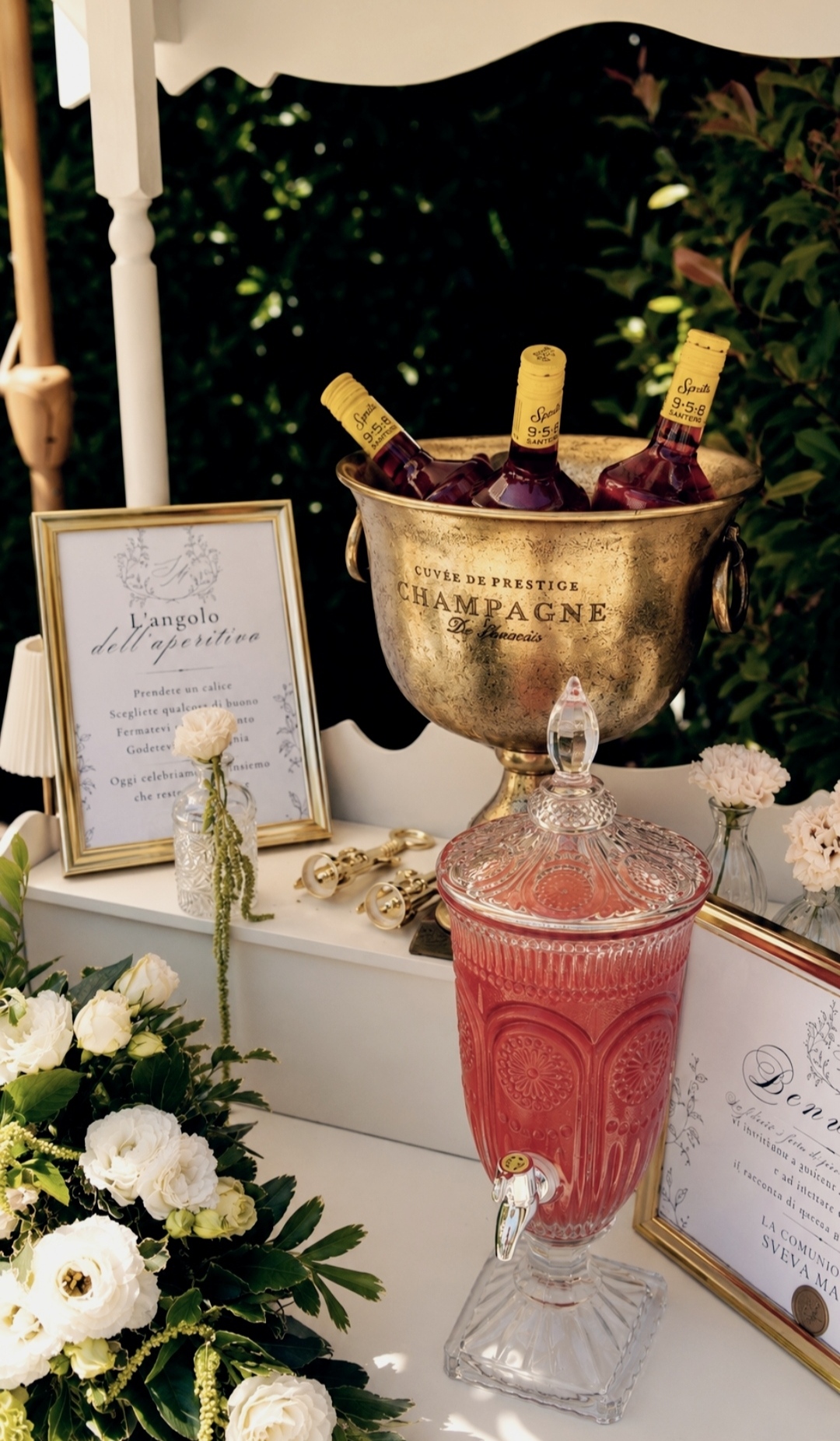 Angolo dell'aperitivo con bevande, fiori bianchi e dettagli dorati nel giardino di Villa Sant'Erasmo