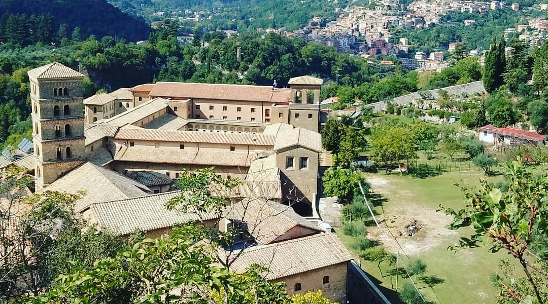 Il Monastero di Santa Scolastica di Subiaco di giorno: la mole in pietra chiara con il campanile romanico a bifore, i tetti in coppi e il chiostro, affacciata sulla vallata boscosa