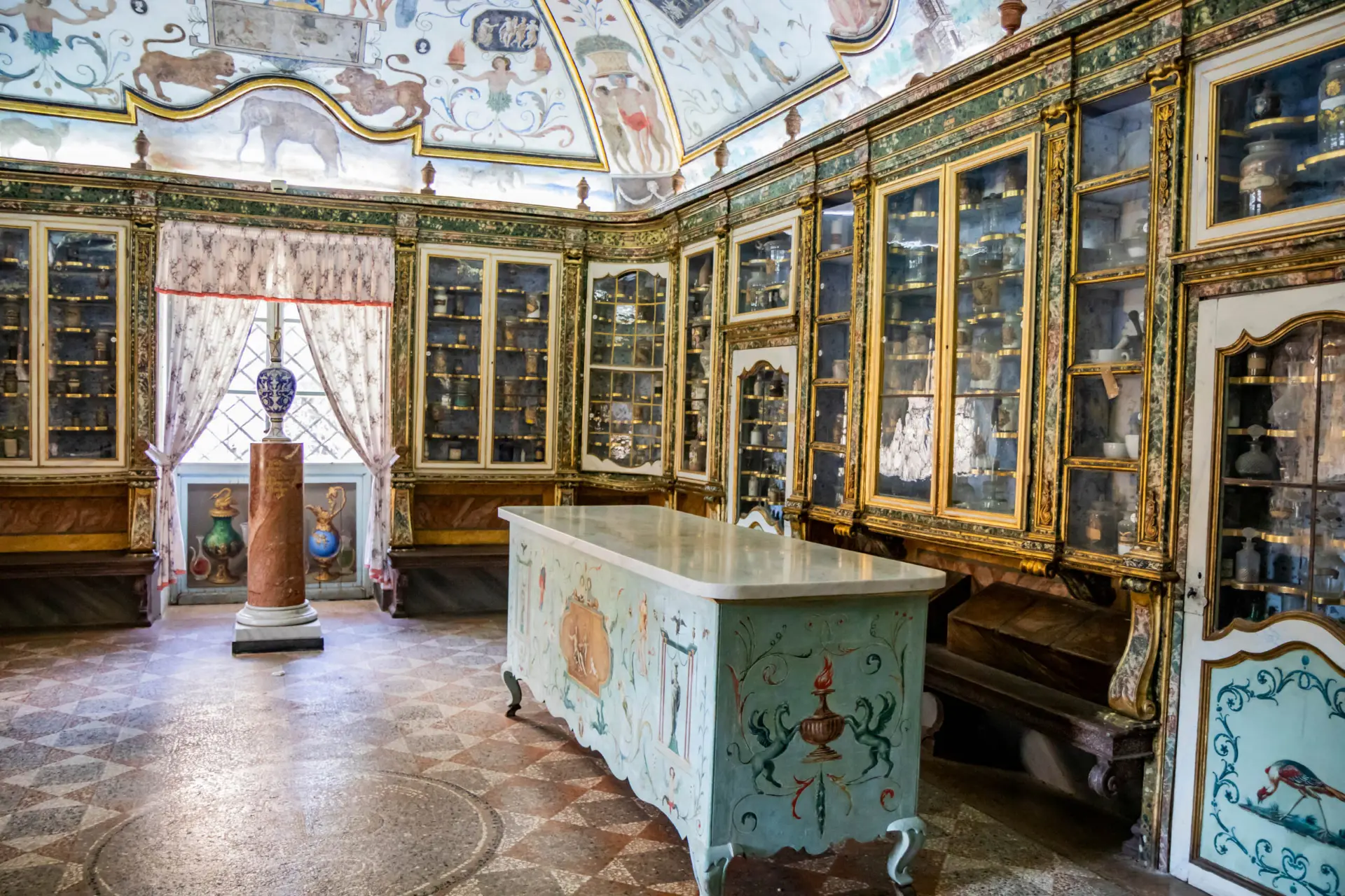 Interno dell'antica farmacia della Certosa di Trisulti con mobili verde scuro e dorature, vetrine di vasi e alambicchi antichi, bancone in marmo e soffitto affrescato a trompe-l'œil