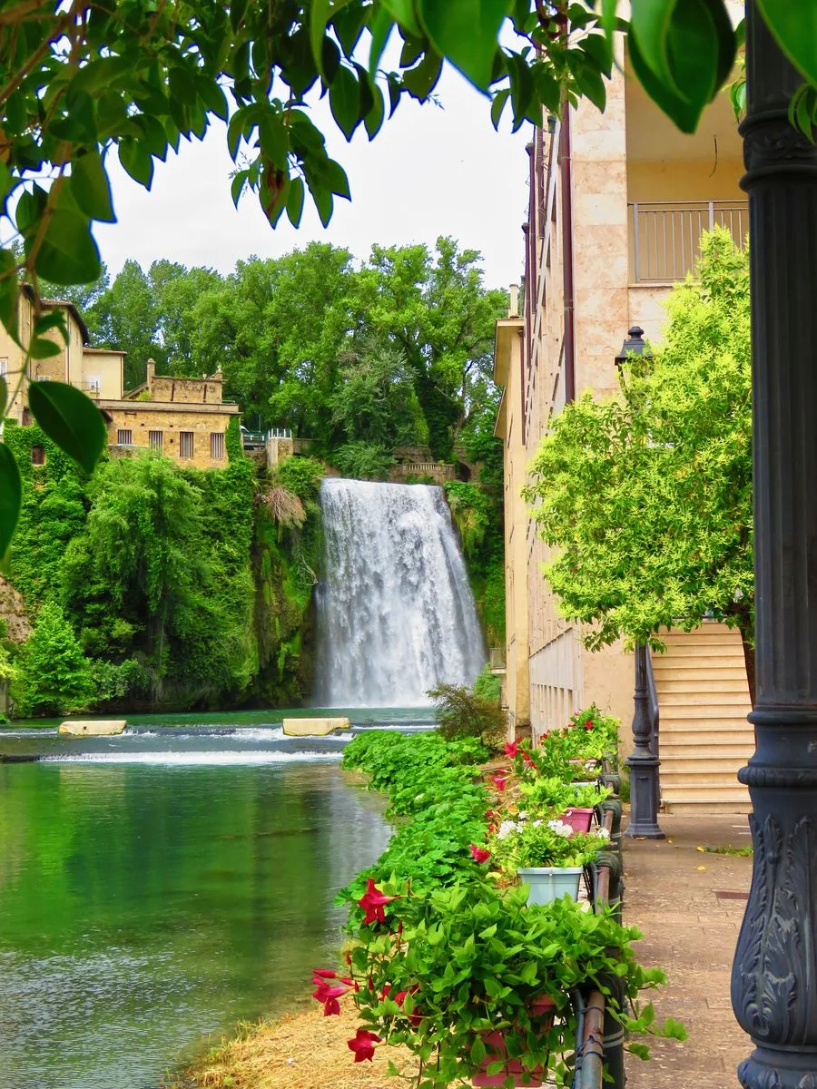La Cascata Grande di Isola del Liri vista dal sentiero lungo il fiume, tra le case in pietra e i fiori della passeggiata