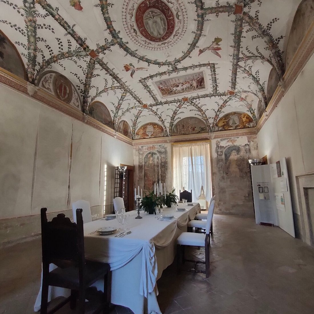 Salone interno della Rocca Abbaziale di Subiaco con volta a crociera affrescata, tavola apparecchiata e tende luminose