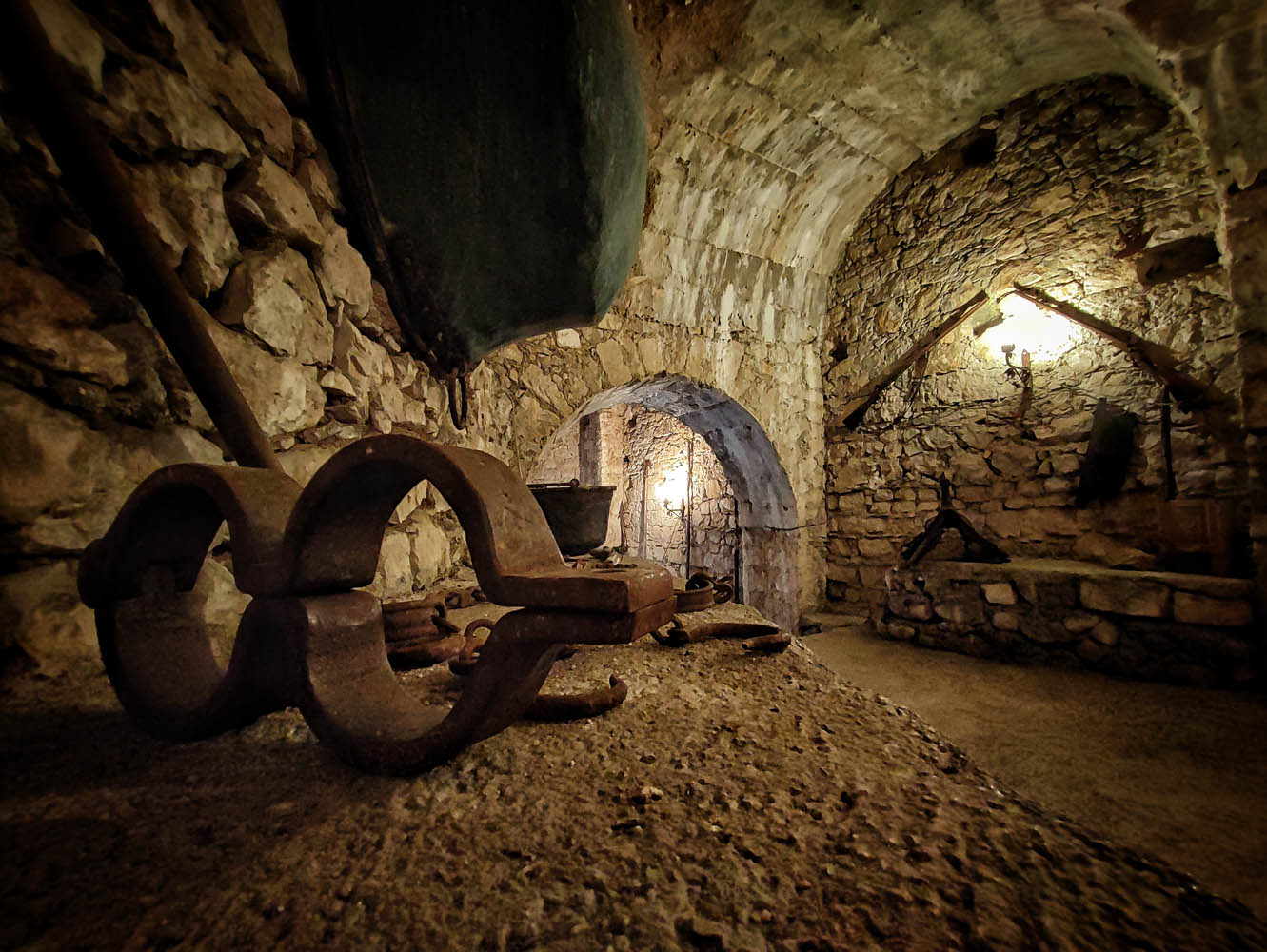 Sotterranei in pietra del Castello di Fumone con ceppi e strumenti antichi illuminati da luce calda