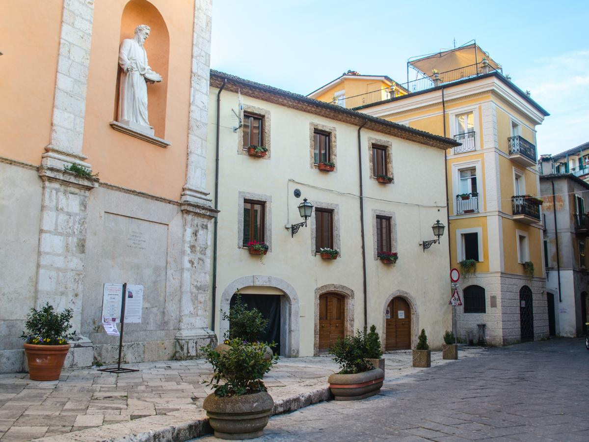 Piazza del centro storico di Isola del Liri con edificii color crema e giallo, statue in nicchia, archi in pietra e vasi di fiori