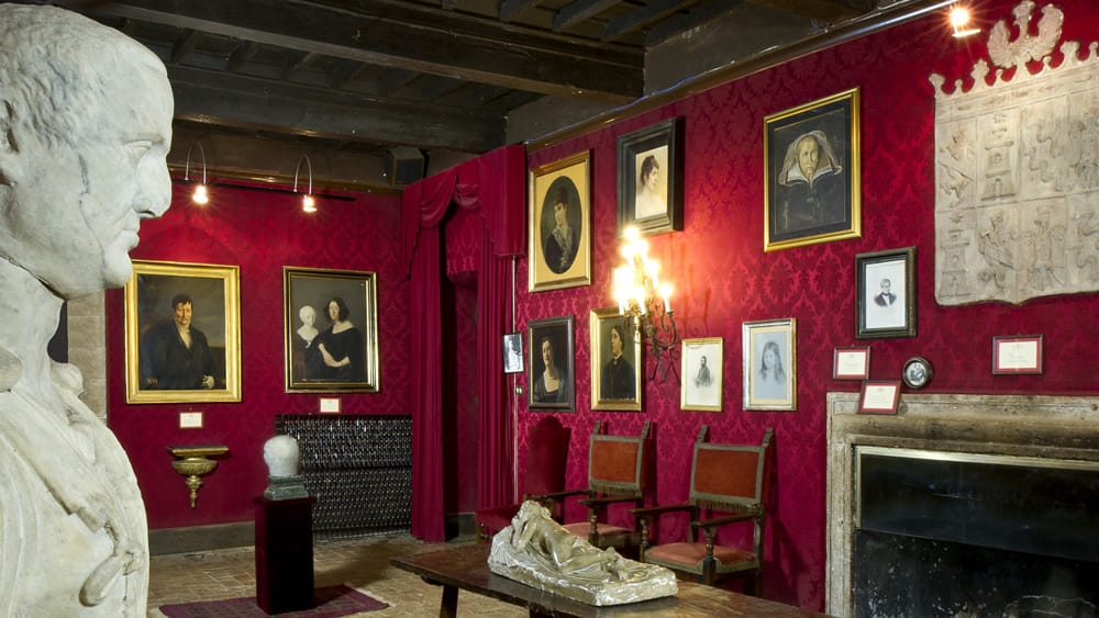 Salone interno del castello di Fumone con pareti in damasco rosso, dipinti antichi e camino in pietra