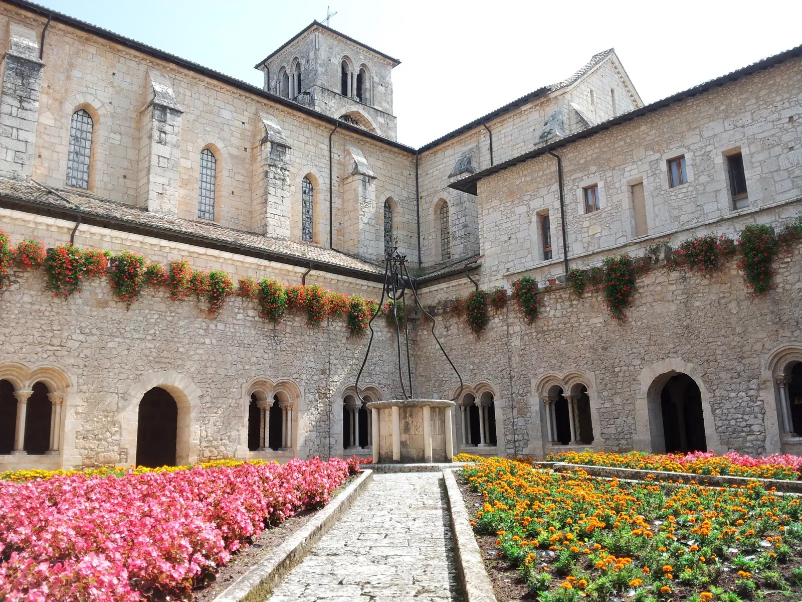 Il chiostro dell'Abbazia di Casamari con il pozzo in pietra al centro, le arcate a colonne binate e le aiuole fiorite di rose e vignali lungo il sentiero