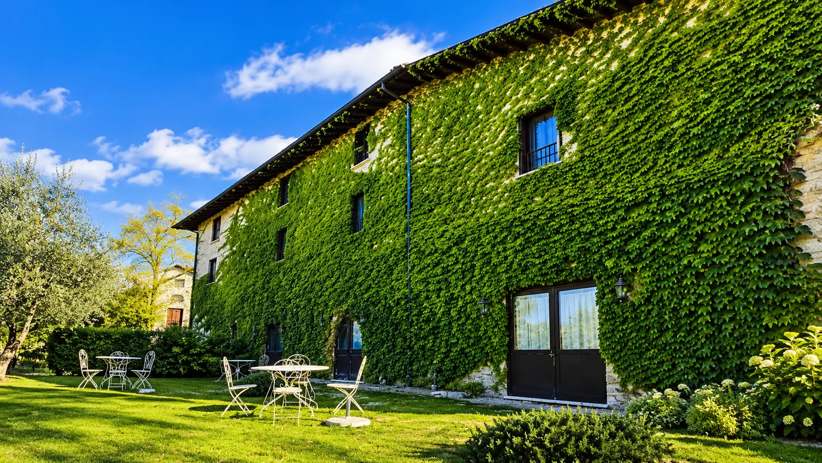 La facciata di Villa Sant'Erasmo ricoperta di edera, con tavolo e sedie da giardino sotto un cielo azzurro