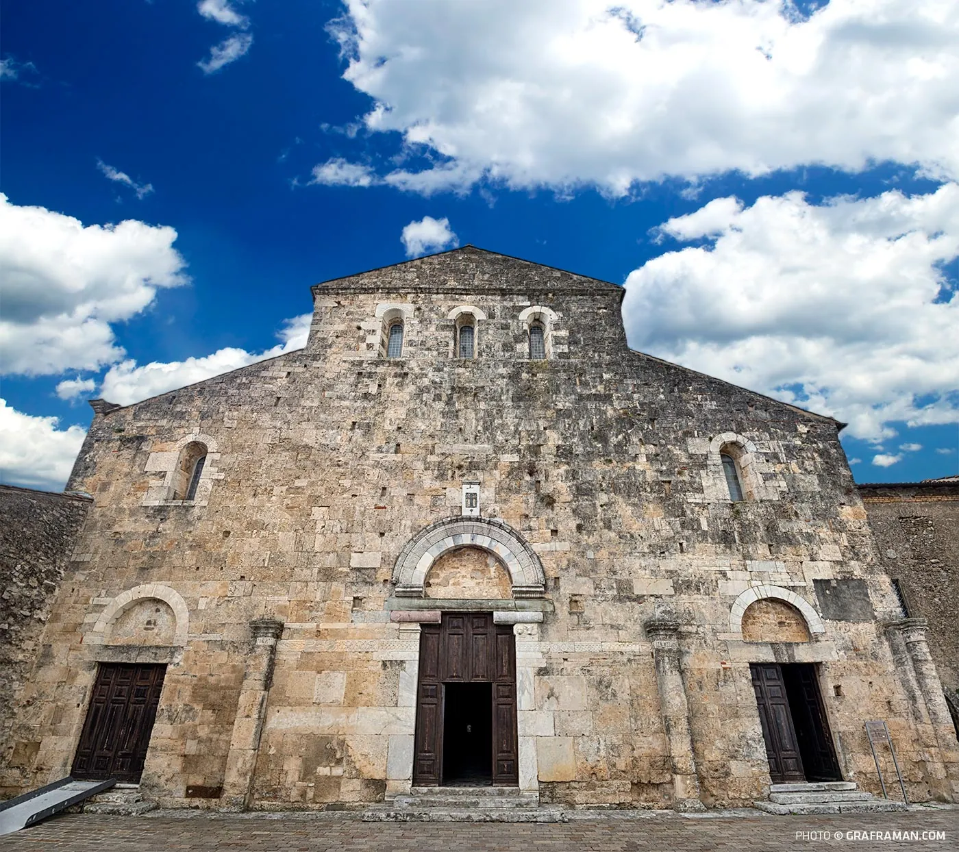 La facciata romanica della Cattedrale di Santa Maria ad Anagni in pietra calcarea con tre portali e rosone sotto cielo azzurro